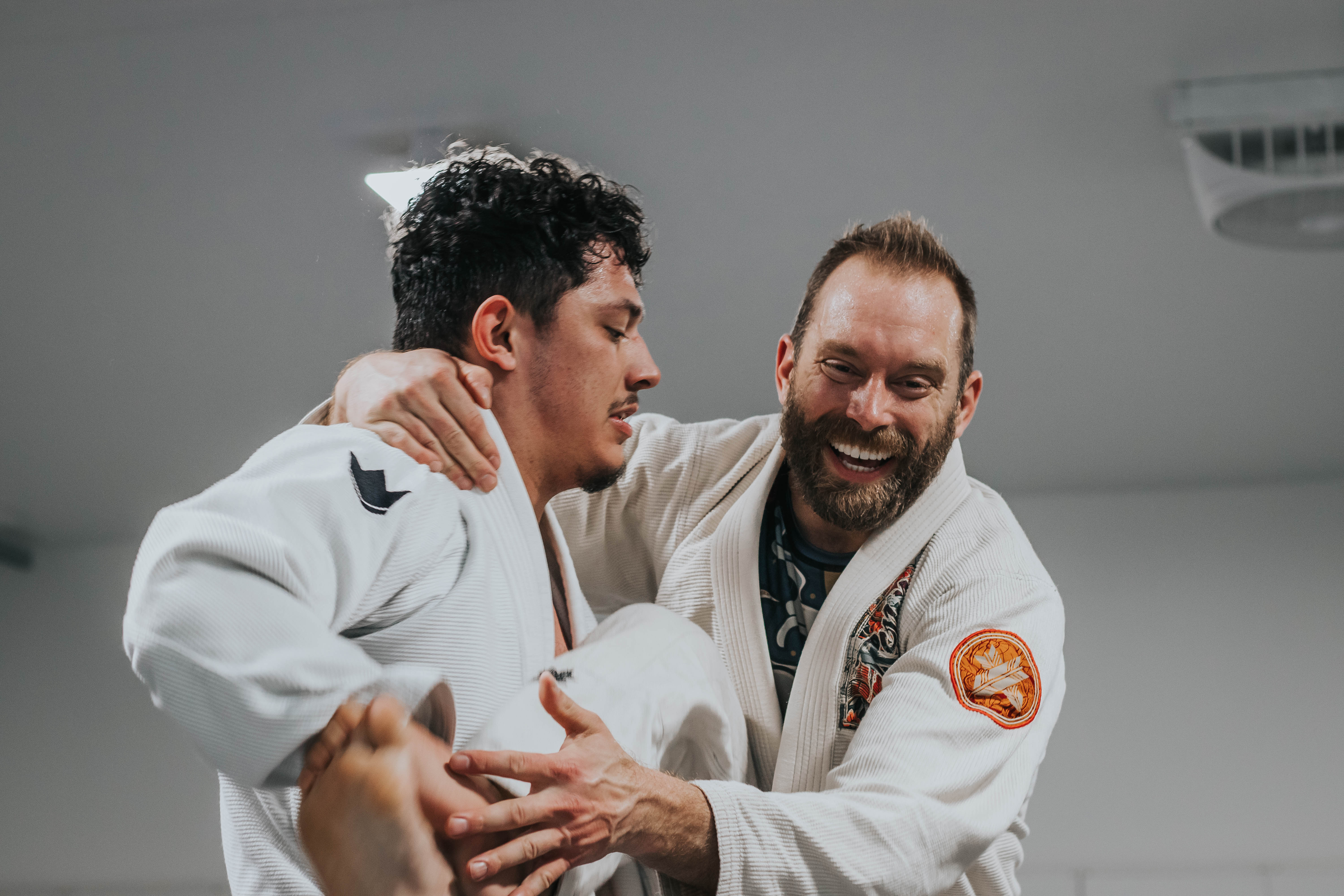 two men laughing while doing takedowns (training jiu-jitsu a martial art of self-defense and self-offense)